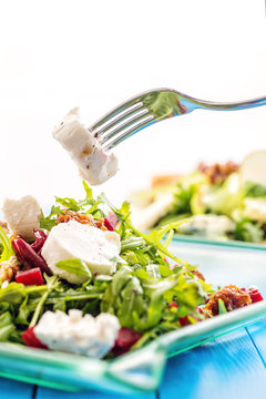 fresh arugula salad with beetroot, goat cheese, bread slices and walnuts with metal fork in hand, product photography for restaurant or healthy lifestyle