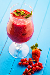 fresh red smoothie with mint leaf in glass on blue background, strawberry, red currant, beetroot and apple drink, product photography for healthy lifestyle