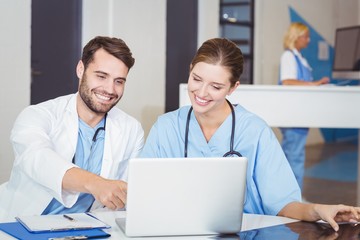 Happy doctors using laptop while discussing at desk