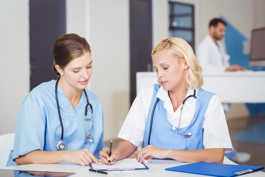 Female doctor writing on paper while discussing with colleague