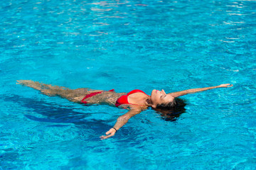 Young woman relaxing in resort swimming pool on summer vacation. Brunette caucasian model in red bikini floating in water.