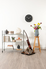 white wall black chair with vase of flower, clock and guitar