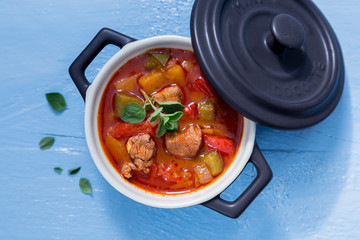 Gulasch in einer schwarzen cocotte mit Majoran auf blauem Holz