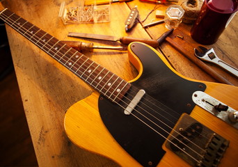 Naklejka premium Guitar on guitar repair desk. Vintage electric guitar on a guitar repair work shop. Single cutaway solid body guitar, amber color. Warm lighting
