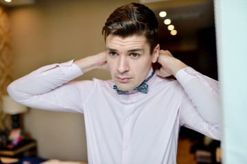 Groom is wearing a bowtie indoors. Male portrait of handsome guy. Beautiful model boy in colorful wedding clothes. Man is posing