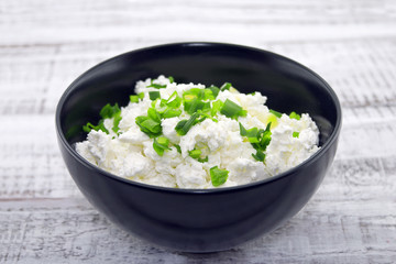 Cottage cheese with chives in black ceramic bowl 