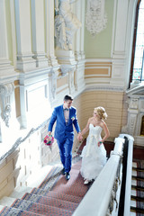 Wedding couple is walking. Beautiful model girl in white dress. Handsome man in suit. Beauty bride with groom. Female and male portrait. Woman with lace veil. Lady and guy indoors