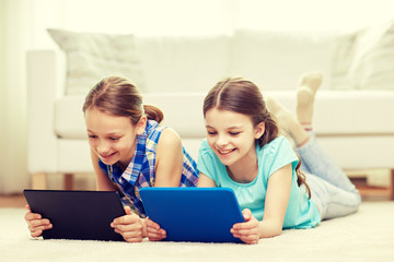 happy girls with tablet pc lying on floor at home