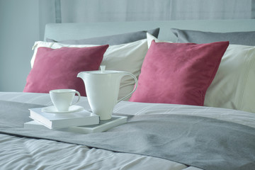 Ceramic tea set and books setting on bed with red velvet pillows