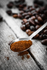 Close up photo of spoon with ground coffee in gray wooden background, coffee beans in second plan.