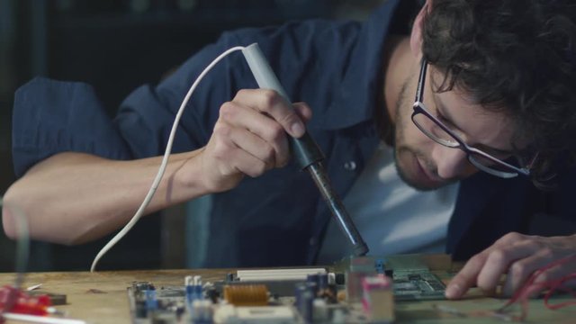 Student is studying electronics and soldering a circuit board in a garage. Shot on RED Cinema Camera.