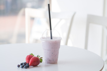 smoothie in plastic cup at the table with strawberry and blackbe