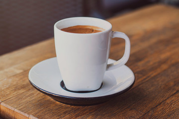 A cup of coffee on a wooden table in cafe, soft warm filter, lens flare 