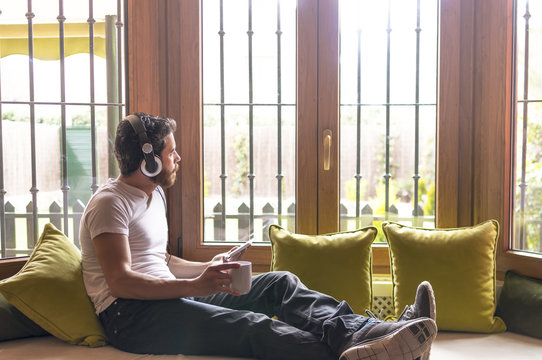 Young man listening music with tablet by the window