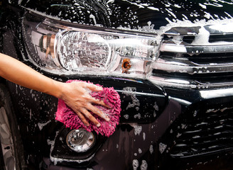 man washing a soapy black car with a cloth