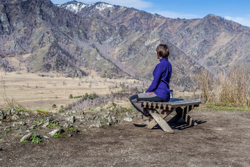Fototapeta na wymiar Young woman sitting on a bench and looking at a mountains with a cup of tea