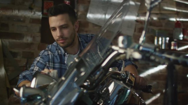 Man is cleaning and polishing chrome objects on his motorcycle in a garage. Shot on RED Cinema Camera.