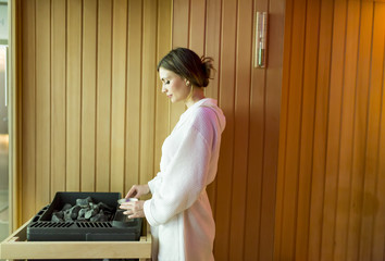 Woman pouring water on the rocks in the sauna