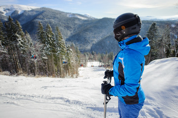 Female skier against ski-lift and winter mountains background. Woman is wearing helmet skiing glasses gloves and blue ski suit. Carpathian Mountains, Bukovel, Ukraine