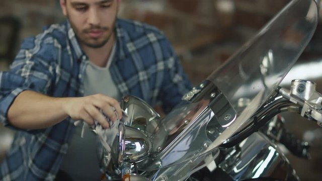 Man is cleaning and polishing chrome objects on his motorcycle in a garage. Shot on RED Cinema Camera.