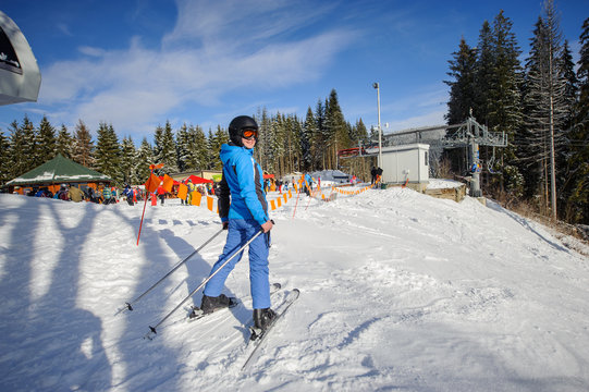 Full length portrait of female skier on the top of ski slope on a sunny day at ski resort. Woman is smiling and looking at the camera. Carpathian mountains. Bukovel, Ukraine