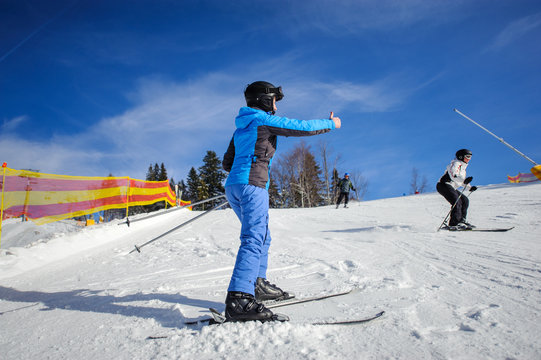 Rear view of female skier on a sunny day at ski resort on a ski slope giving the thumb up. Winter sports concept. Carpathian Mountains, Bukovel