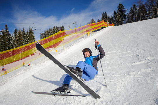 Happy girl skier in blue ski suit after the fall on mountain slope. Ski resort. Winter sports concept. Carpathian Mountains, Bukovel, Ukraine
