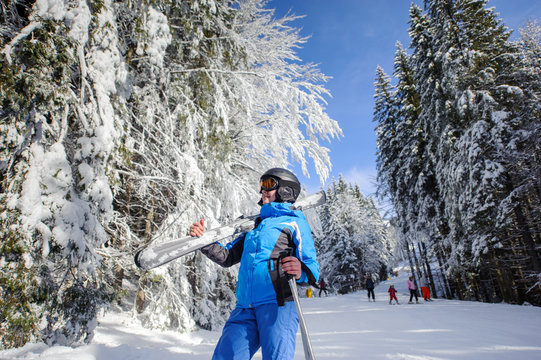 Portrait of active happy female skier on a ski slope in the winter forest on a sunny day. Woman is holding skis on her shoulder. Ski resort. Wide angle. Bukovel, Ukraine