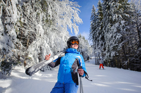 Portrait of young happy female skier on a ski slope in the winter forest on a sunny day. Woman is holding skis on her shoulder. Ski resort. Carpathian Mountains, Bukovel, Ukraine