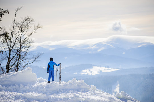Rear view of skier standing on top of the mountain and enjoying the view on beautiful winter mountains on a sunny day. Winter sports concept.