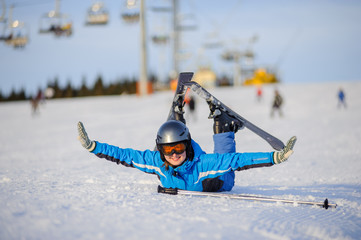 Fototapeta na wymiar Young beautiful female skier in blue ski suit orange goggles and helmet lying on the snow and having fun at ski resort at Carpathian Mountains on a sunny day. Ski vacation.