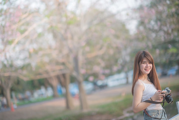 beautiful asian woman photographer holding camera seat Standing behind a tree with sunset time (selective focus)