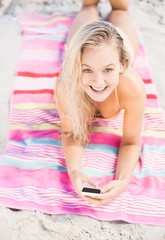 Obraz na płótnie Canvas Happy woman lying on the beach and using mobile phone