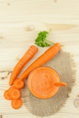 Glass of carrot juice and carrots on the wooden table. Healthy juice full of vitamins and fiber. Diet Food. Carrot segments on a wooden background.
