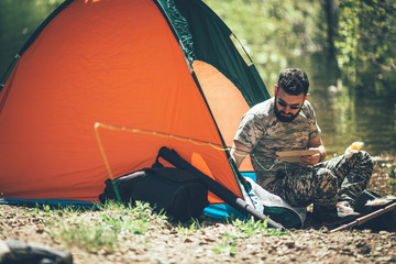 Fly fisherman in camouflage sitting next to the river in his tent and setup fishing rod. © BalanceFormCreative