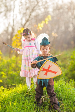 Cute little children dressed up as a knight and a fairy playing in the woods