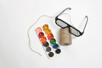 Top view art scene featuring of thread twine, glasses and watercolor paints on a white background. 
