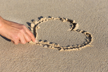 Female hand drawing shape of heart on sand