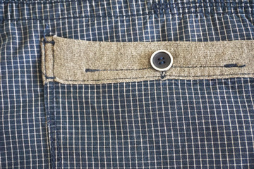 Right pocket with a button on the blue shorts male in a white cage. Pocket with a brown stripe - fashion background 