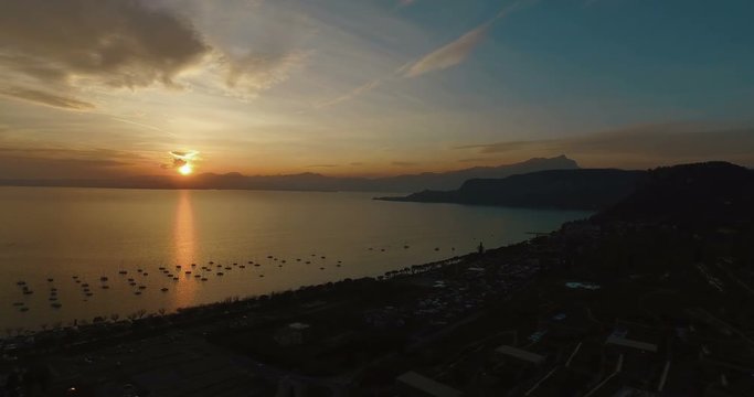 Aerial view on wonderful panoramic view on sunset over beautiful lake Garda (Lago di Garda) with mountains, yachts and sailingboats in Bardolino harbor (Verona, Italy). 