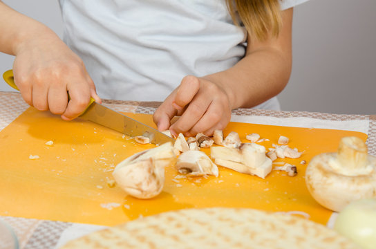 Close-up of childrens hands, cutting knife mushrooms on a cutting board