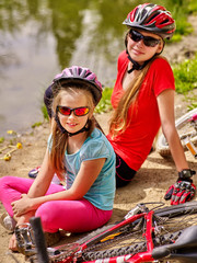 Naklejka premium Bikes cycling family. Happy mother and daughter rides bicycle. Family have rest near water in park. Bicycles are on coast. Active outdoor recreation.