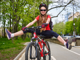 Bikes bicyclist girl. Girl wearing bicycle helmet and glass with rucksack ciclyng road bicycle. Girl  cycling feet up.Girl rides on  bike lane with legs apart.  There is sidewalk at background. Front