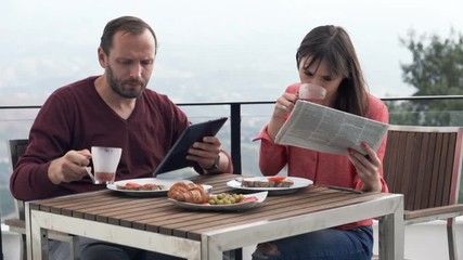Young couple with tablet newspaper sitting during breakfast on terrace 
 - Powered by Adobe