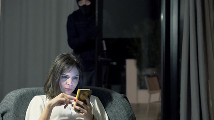 Young woman sitting with smartphone in her home when man in balaclava attack her
- Powered by Adobe