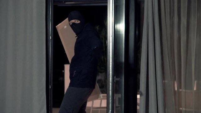 Man in balaclava stealing painting from someone`s house
