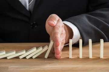 Businessman Stopping Dominoes From Falling