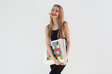 Front view portrait of young female artist holding the hand drawn pictures pack, smiling with a pencil in her teeth.