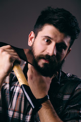 Shaving with axe. Confident young bearded man carrying a big axe on shoulder and looking at camera while standing against dark background