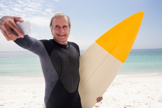 Happy senior man taking selfie with surfboard